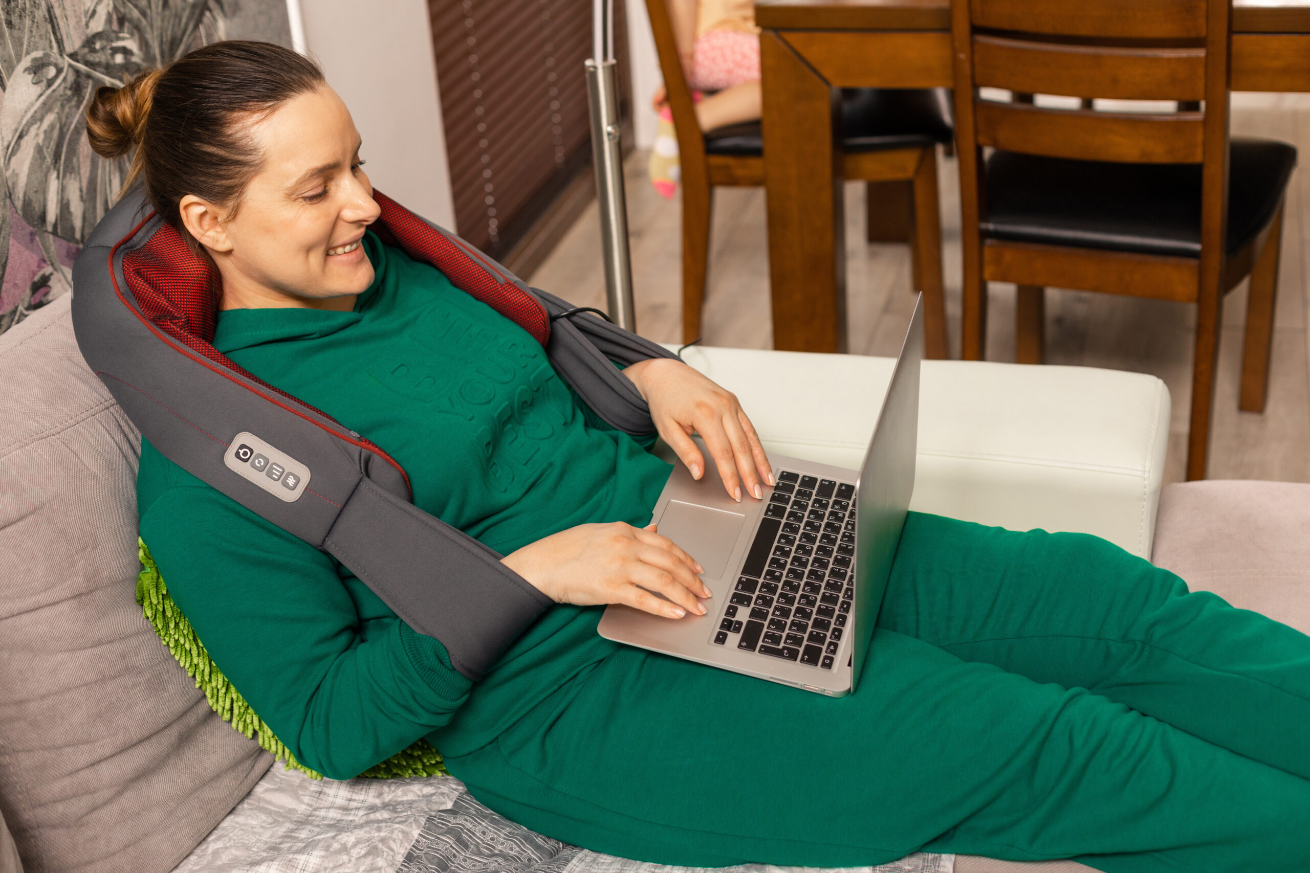 Woman works at home using laptop and enjoys shoulder and neck massage with electric appliance. osteochondrosis. smiles and gets positive emotions.
